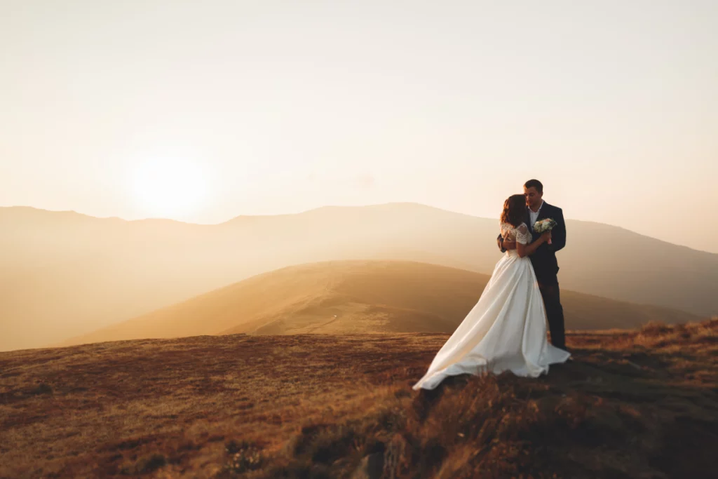 A newlywed couple standing on a mountain side over looking a misty valley in the golden light of dusk