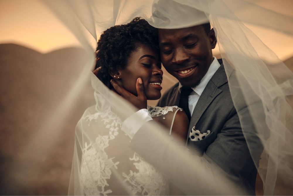 couple getting photo taken under veil looking happy