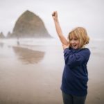 Little girl standing on the beach with her arm upraised in a closed fist