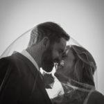 Black and White image of bride and groom under wedding veil smiling