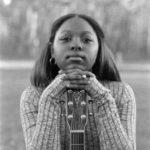 young woman with hands crossed over guitar in black and white
