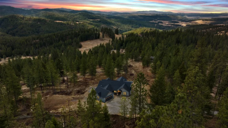An aerial shot of a home in the middle of the woods under a sunset.