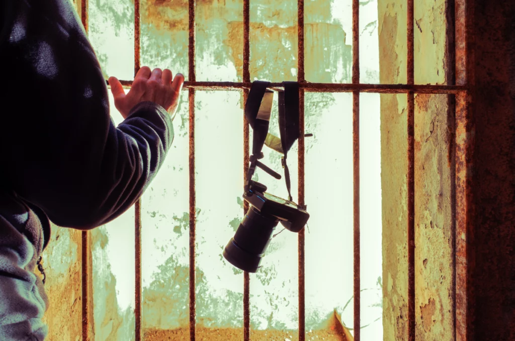 View from inside a rusty old jail cell with a DSLR camera and strap wrapped around a bar.