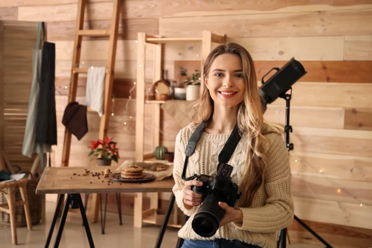 A woman in her home photography studio holding a camera.
