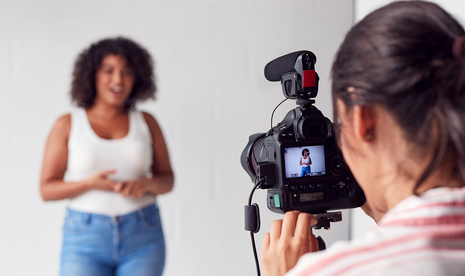 A close-up look at a videographer's camera as she films a client speaking in a studio with a white background.