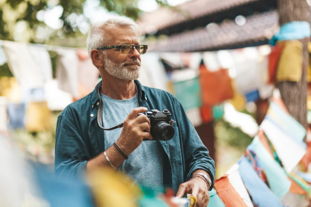 A photographer with his camera in an out-of-focus outdoor space covered in strings of colorful square cloths.