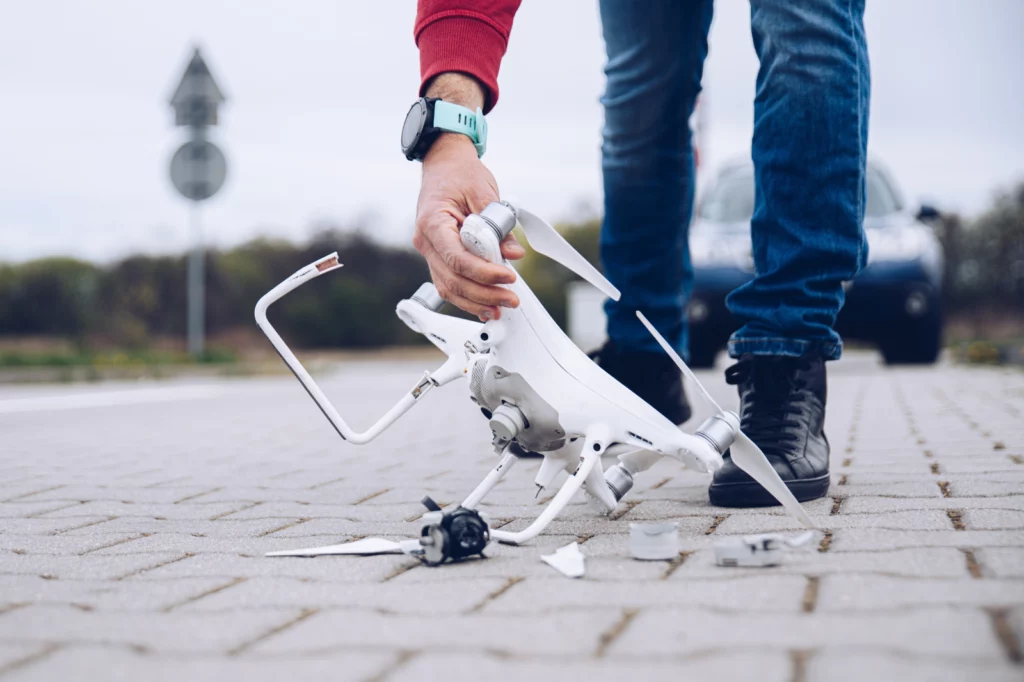 Mans arm reaching down to pick up broken drone on concrete