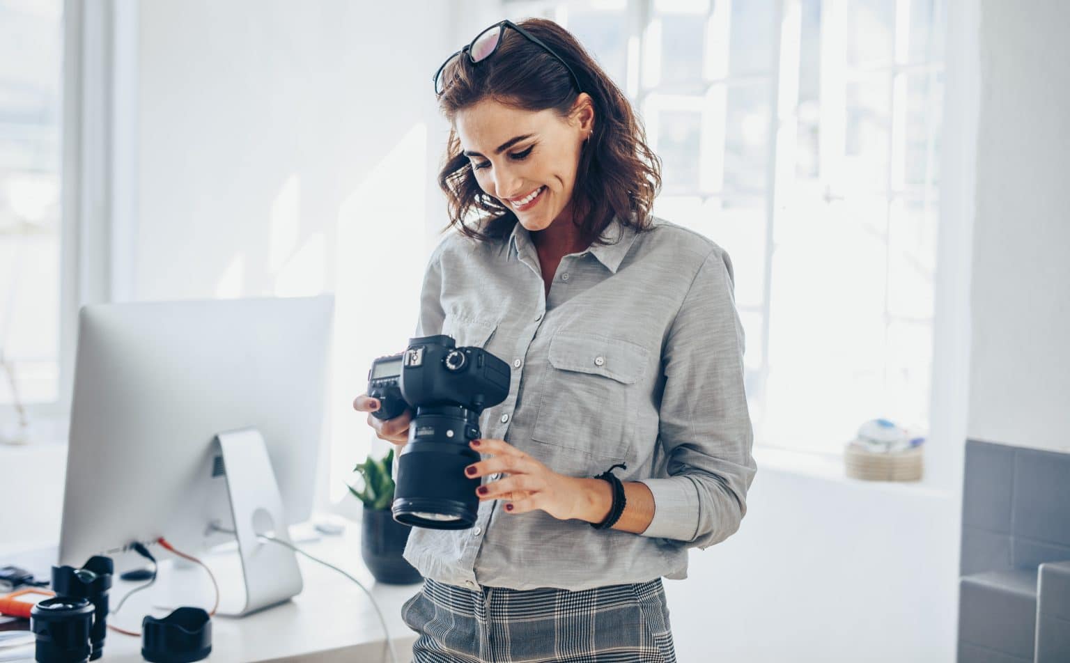 Female photographer checking pictures on camera and smiling. Caucasian woman in casuals standing in her office looking at the photos on her dslr camera.