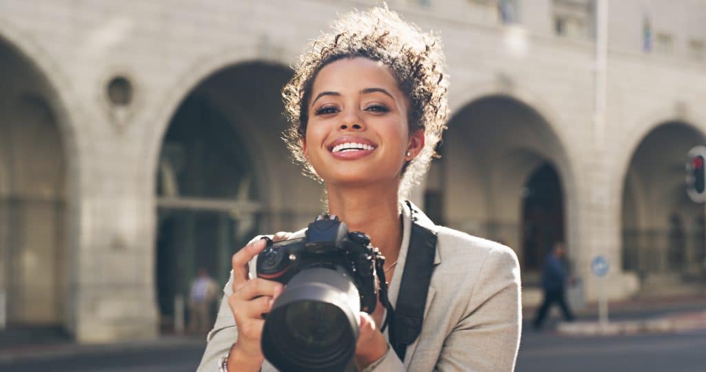 Cropped shot of an attractive young woman standing alone in the city and using her camera to take pictures